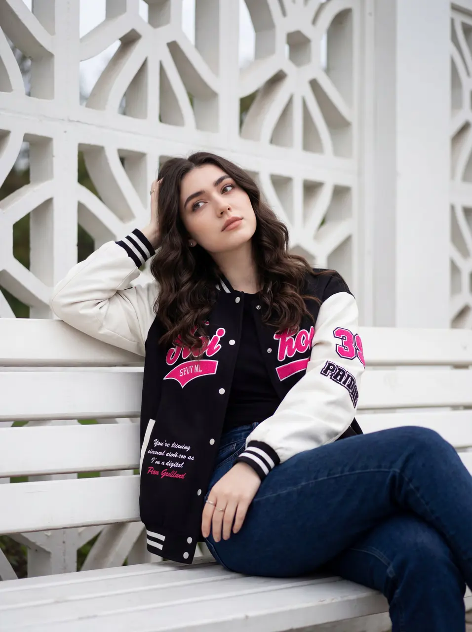 A young woman is sitting casually on a white wooden bench...