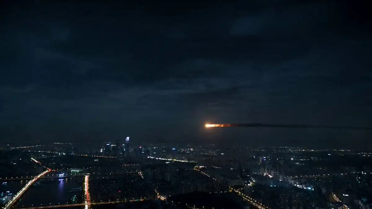 A glowing asteroid enters the atmosphere above a sprawlin...