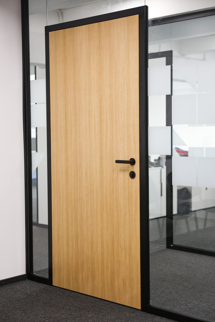 Black aluminium-framed glass door leaf in a glazed partition