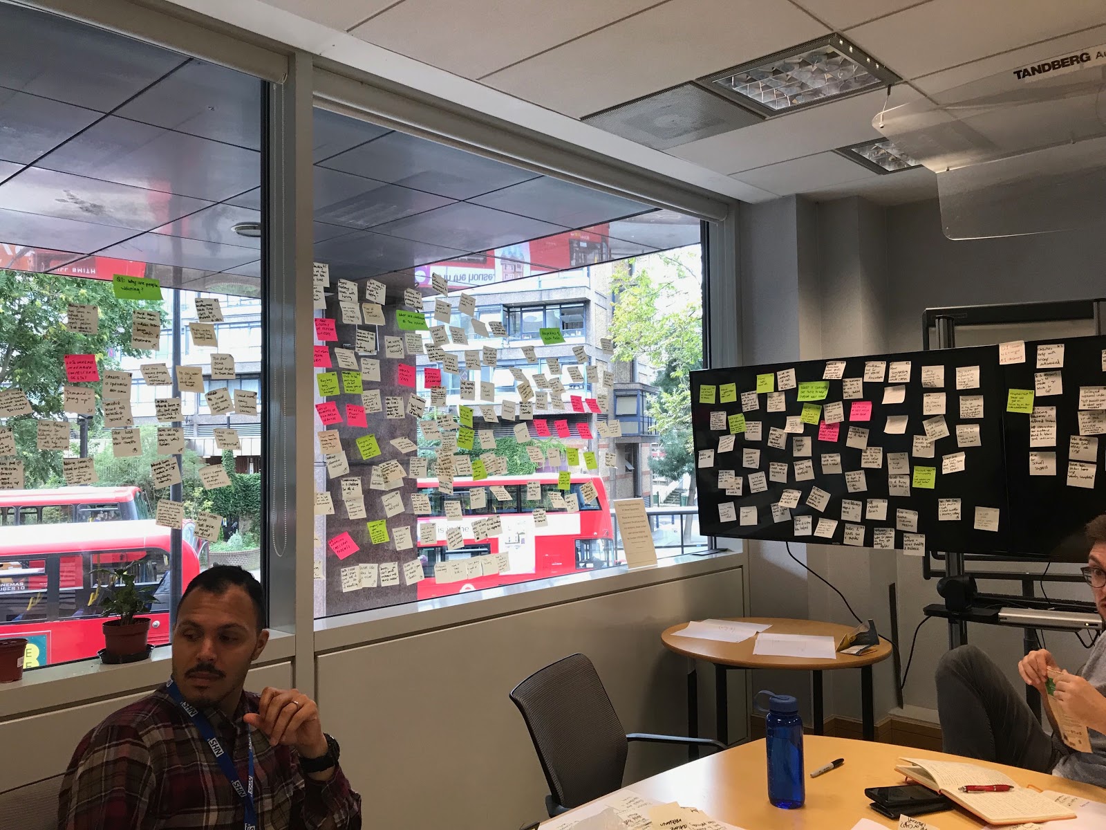 Two team members in a room with post it notes on windows and screens