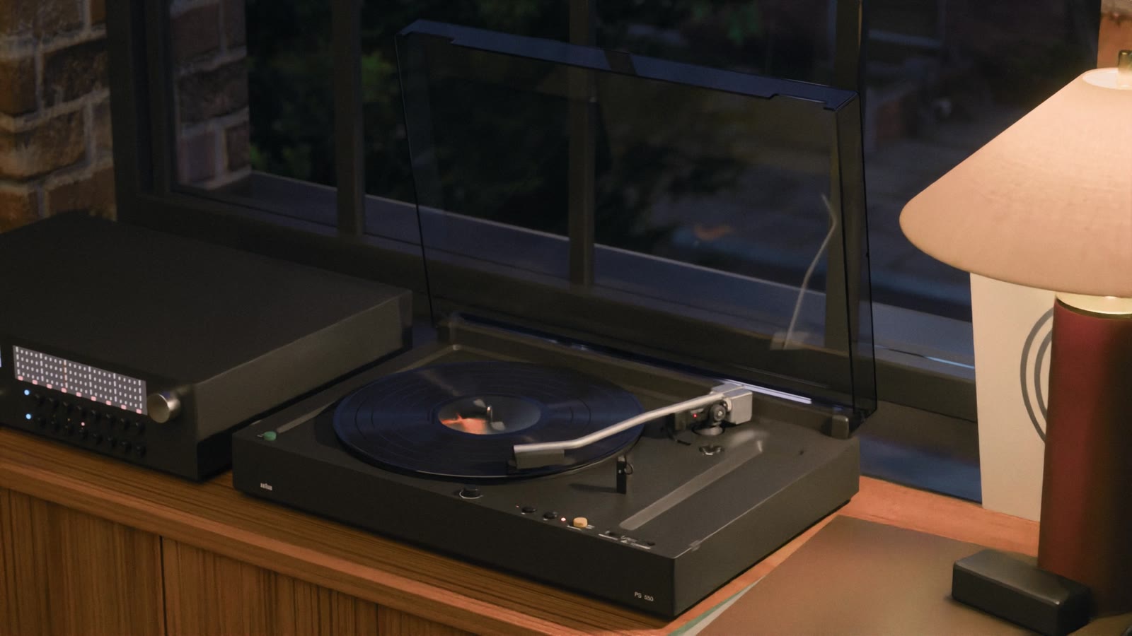 A 1976 Braun PS 550 turntable at night, lid up, a lamp on beside it. A frame from the film made with this skill.