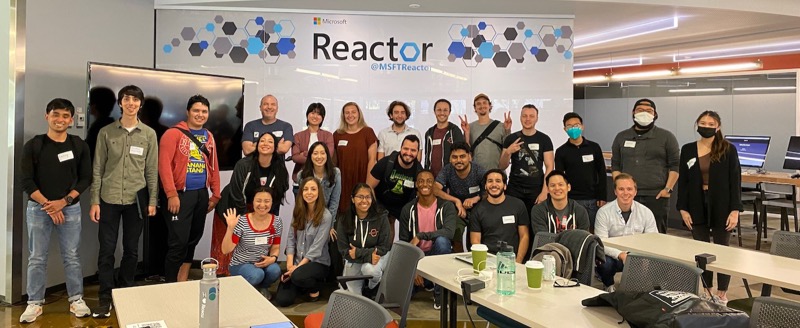 A photo of 24 people standing in front of a whiteboard with a banner saying Reactor. Most of the people are smiling, some are waving