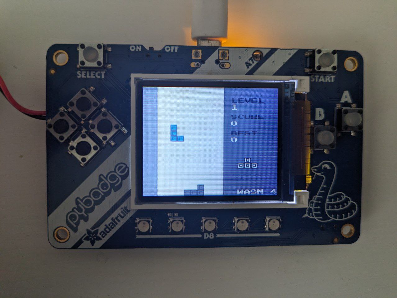 A photo of AdaFruit Pybadge running watris, a Tetris game ported to WASM-4