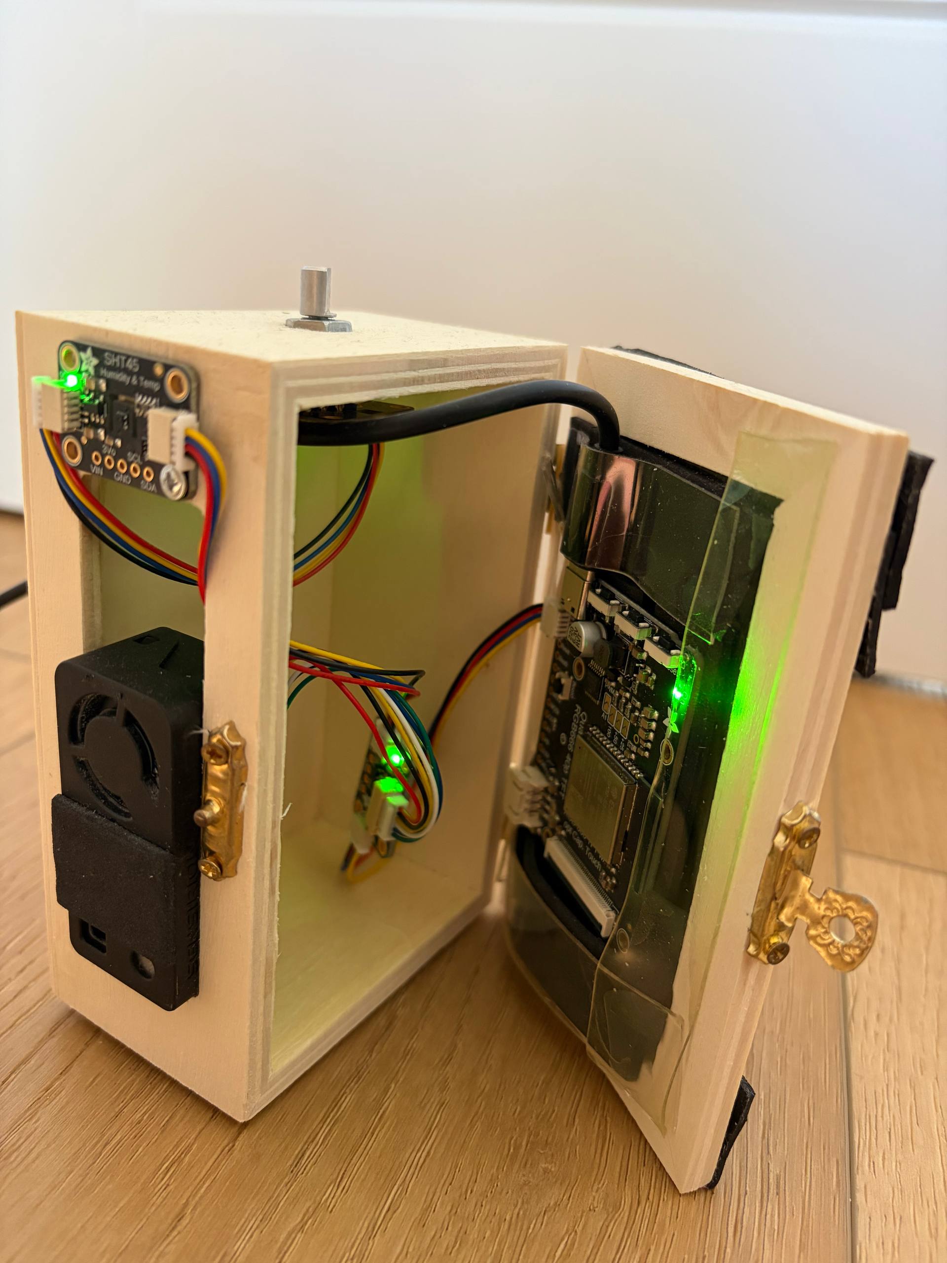 Wooden box opened like a book. SHT45 and SEN66 on the left wall, Qualia S3 board taped to the back of the display in the door, colored STEMMA QT cables inside.