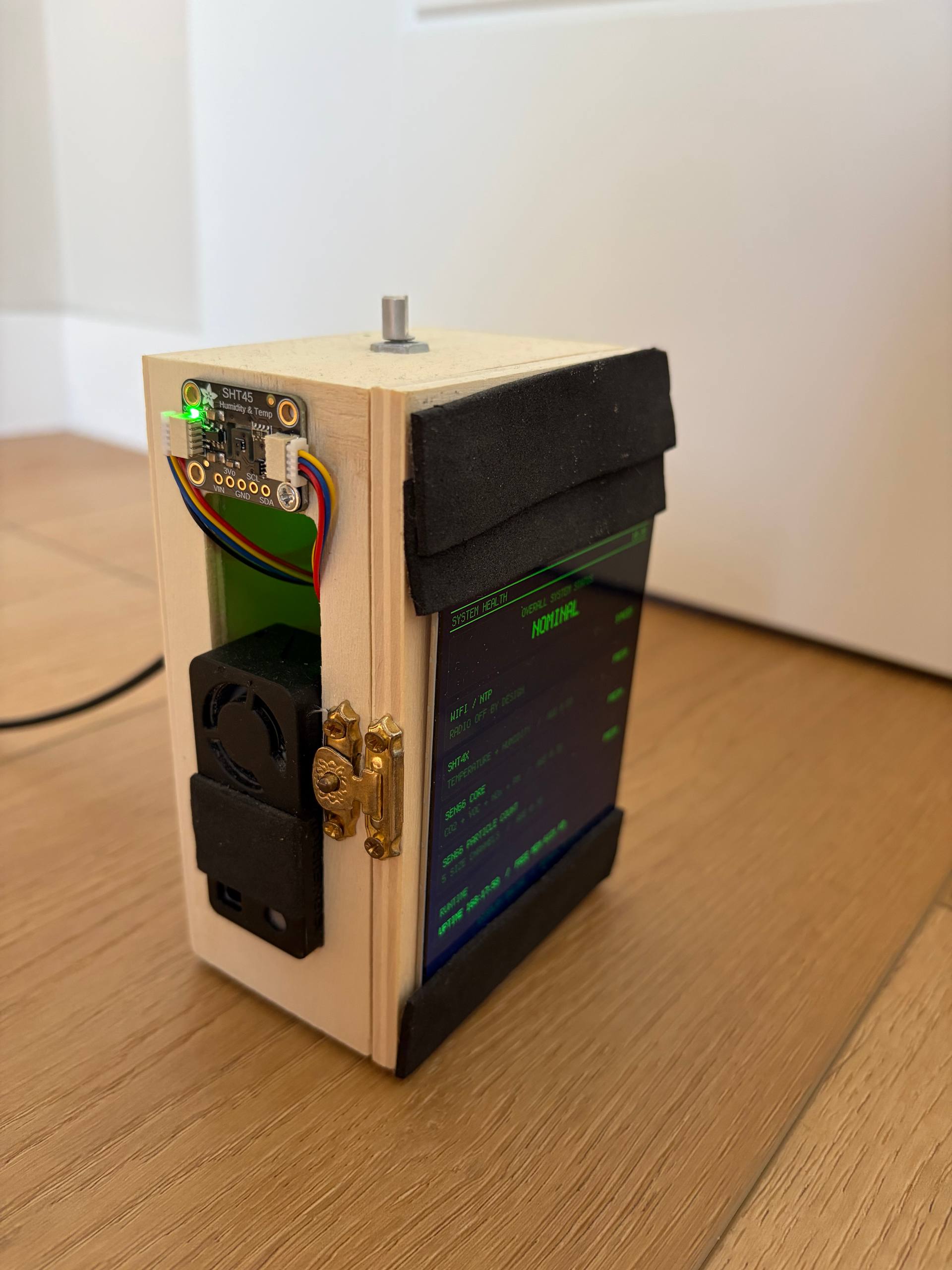 Side of the closed wooden box with the SHT45 board and the black SEN66 sensor mounted outside, a brass latch, and the knob shaft on top.