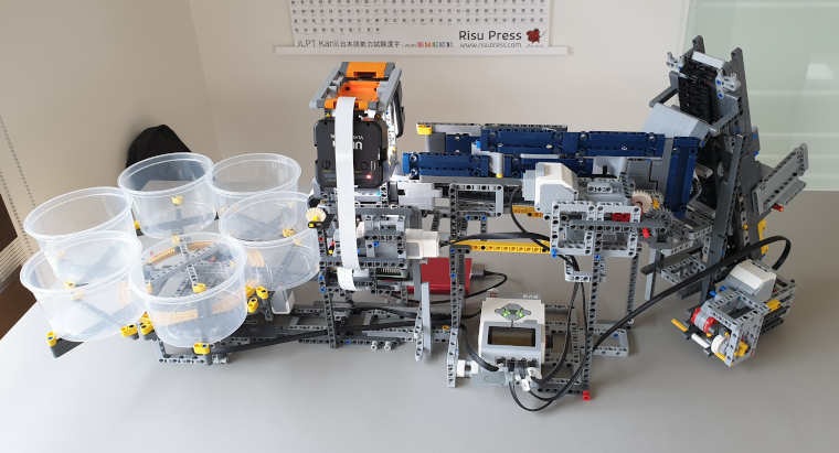 A picture of the built machine, going from right to left: a hopper feeds the bricks into a belt that moves them to a camera, ending up in a wheel consisting of 6 buckets where the sorted bricks are stored