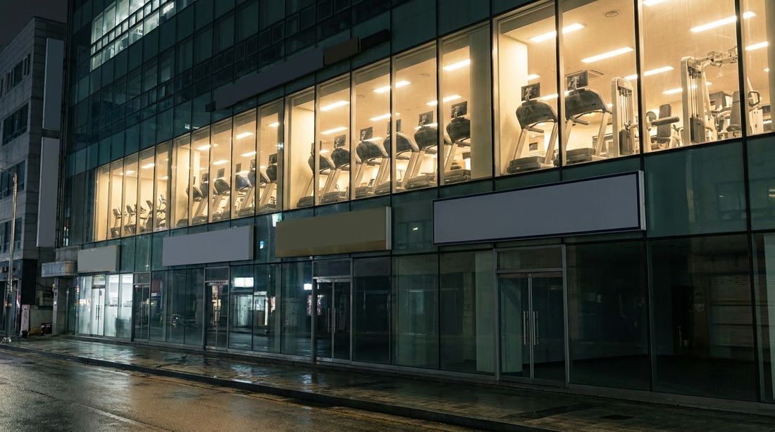 A 24-hour gym lit up on an upper floor above a Seoul street at night
