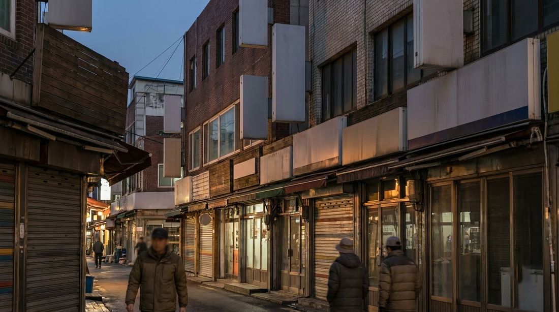 A row of small storefronts in a dense Korean commercial street at dusk