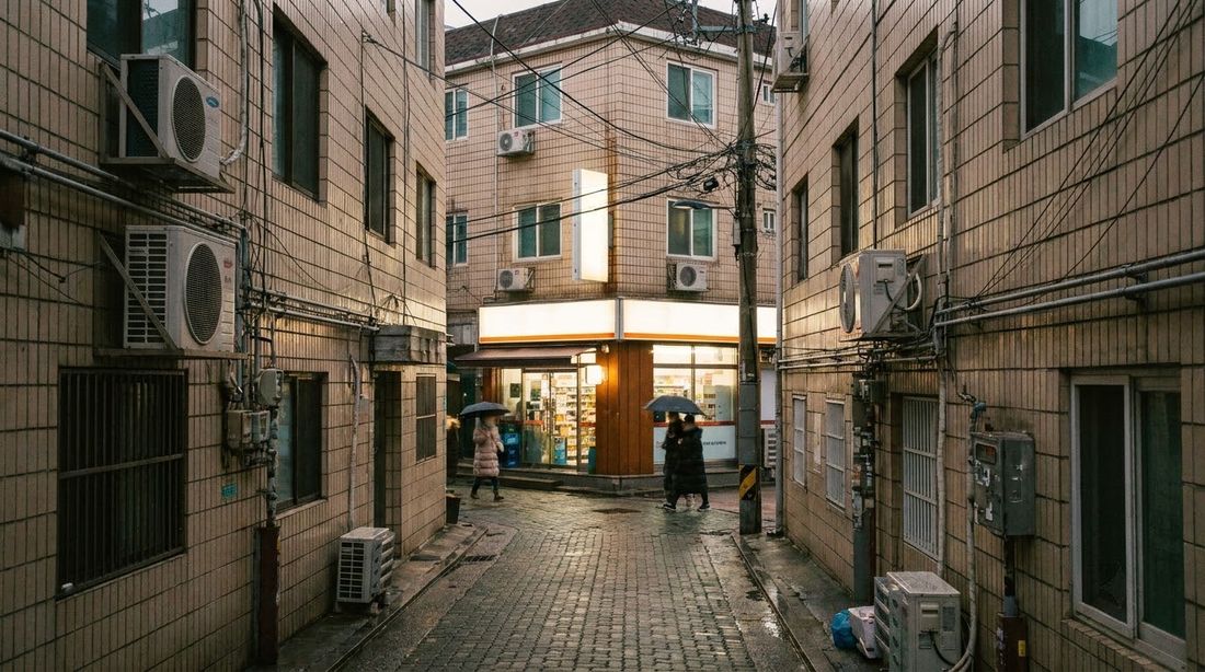 A narrow Seoul residential alley at dusk with a lit convenience store on the corner