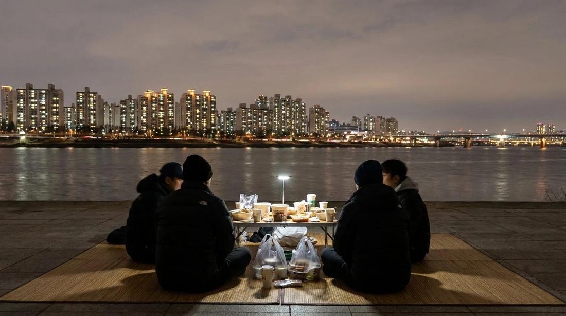 A riverside picnic blanket at night with the city across the water
