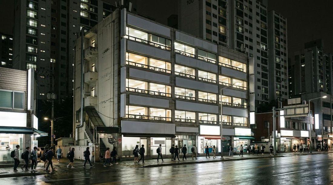 A stacked block of private academies lit at night beside apartment towers