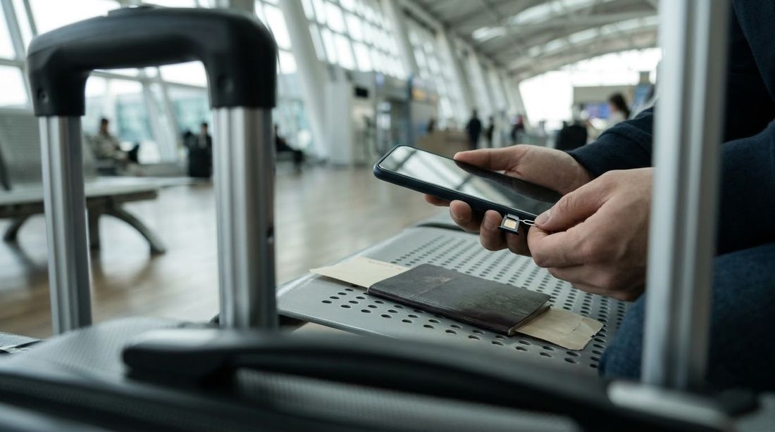 A traveler's hands opening a smartphone SIM tray on an airport bench beside a passport
