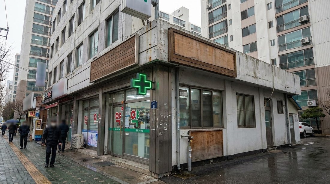 A small neighborhood pharmacy on a Korean street with a green cross sign above the door