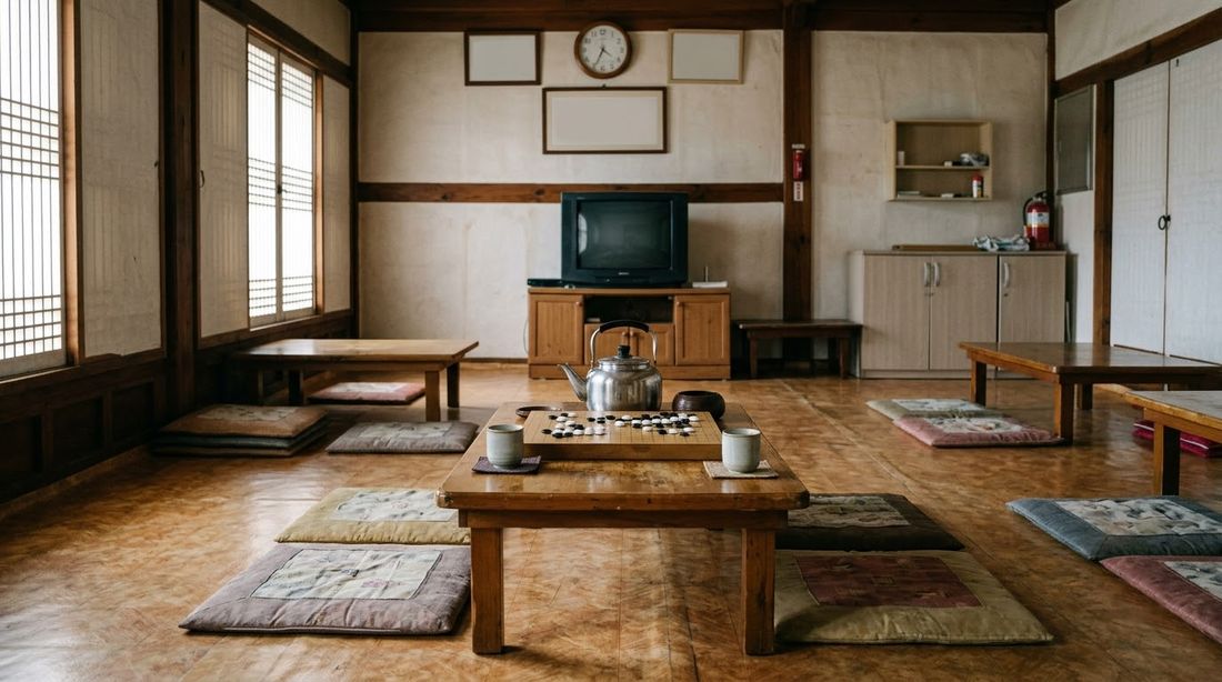 The interior of a modest Korean senior hall: low tables with floor cushions, a baduk board and an old television