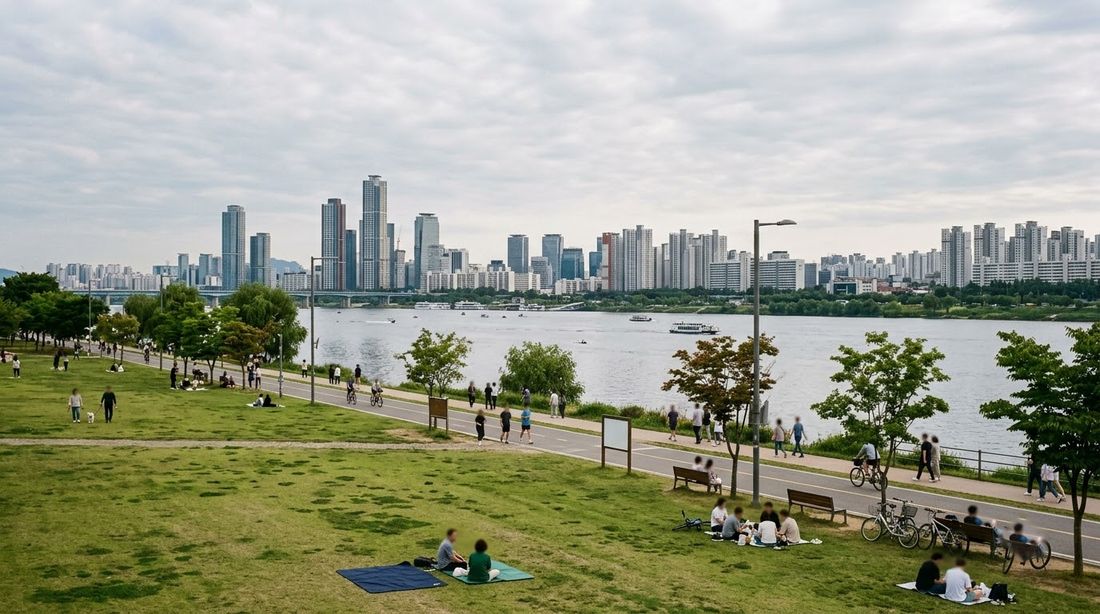 A riverside lawn and walking path along the Han River in Seoul with the city skyline across the water