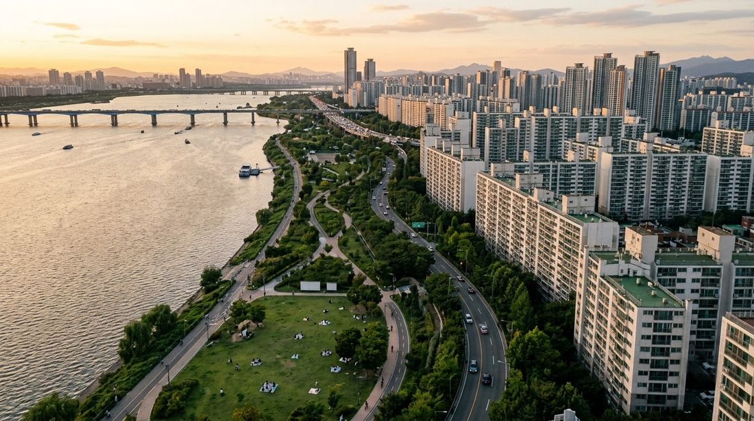 Golden-hour aerial view of the Han River park running between the water and rows of Seoul apartment towers