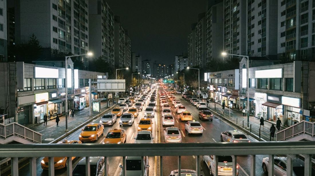 A wide Korean arterial road at night seen from a pedestrian overpass, taxis in the traffic