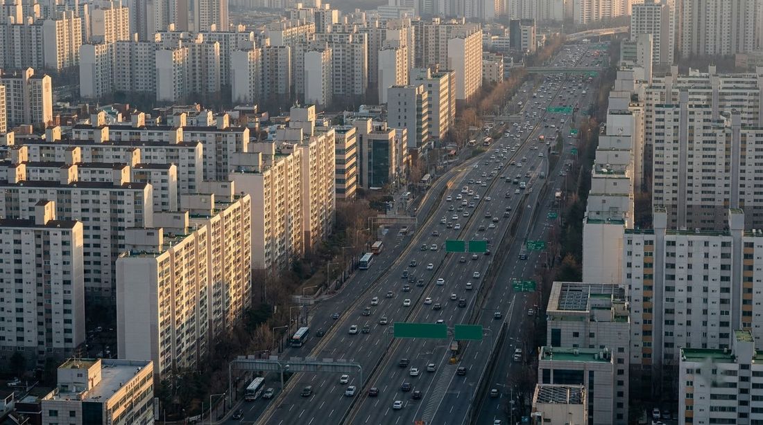 Elevated golden-hour view of a wide road cutting between dense Korean apartment towers
