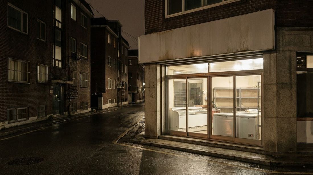 An unstaffed Korean neighborhood shop lit from inside late at night, freezers visible through the glass front