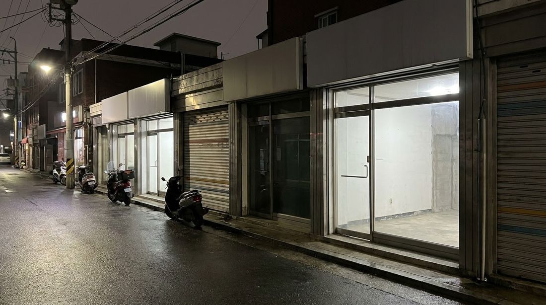 A Korean neighborhood commercial street after midnight, roll-down shutters closed on most units