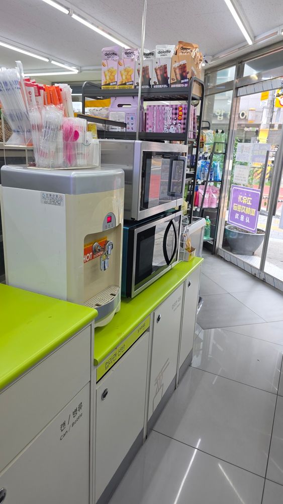 Hot water dispenser, two microwaves, free utensils and sorting bins inside a Korean convenience store