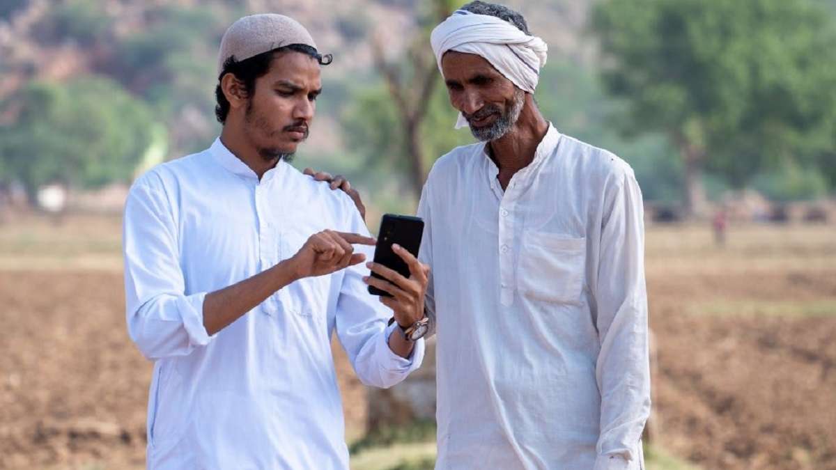 One Indian farmer pointing out something to another on his mobile phone