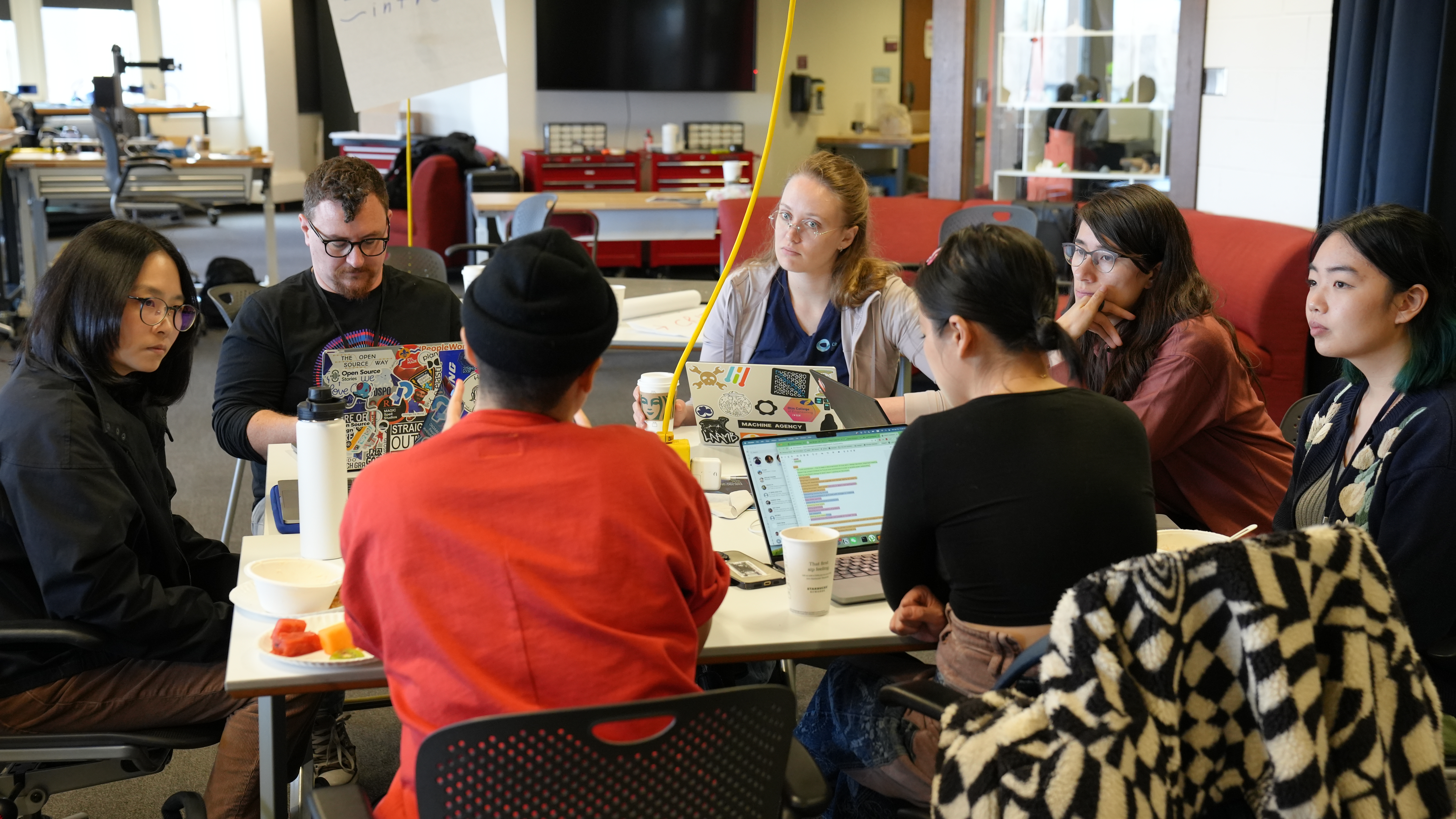 Image description: A group of people around a table, with laptops open and everyone listening intently. Photo by Chris Coleman