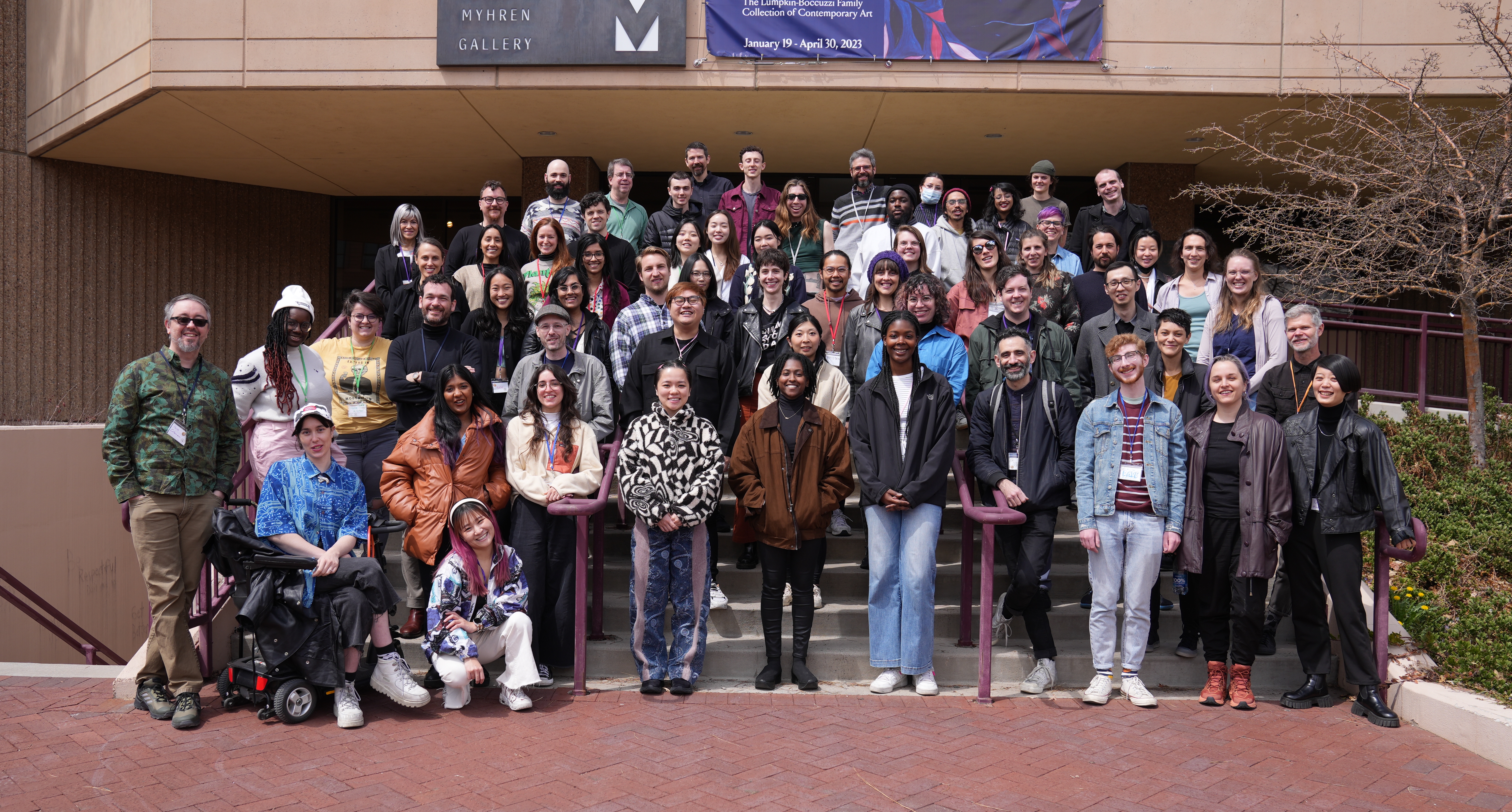 Image description: Approximately 70 people standing or sitting at front of a building smiling.