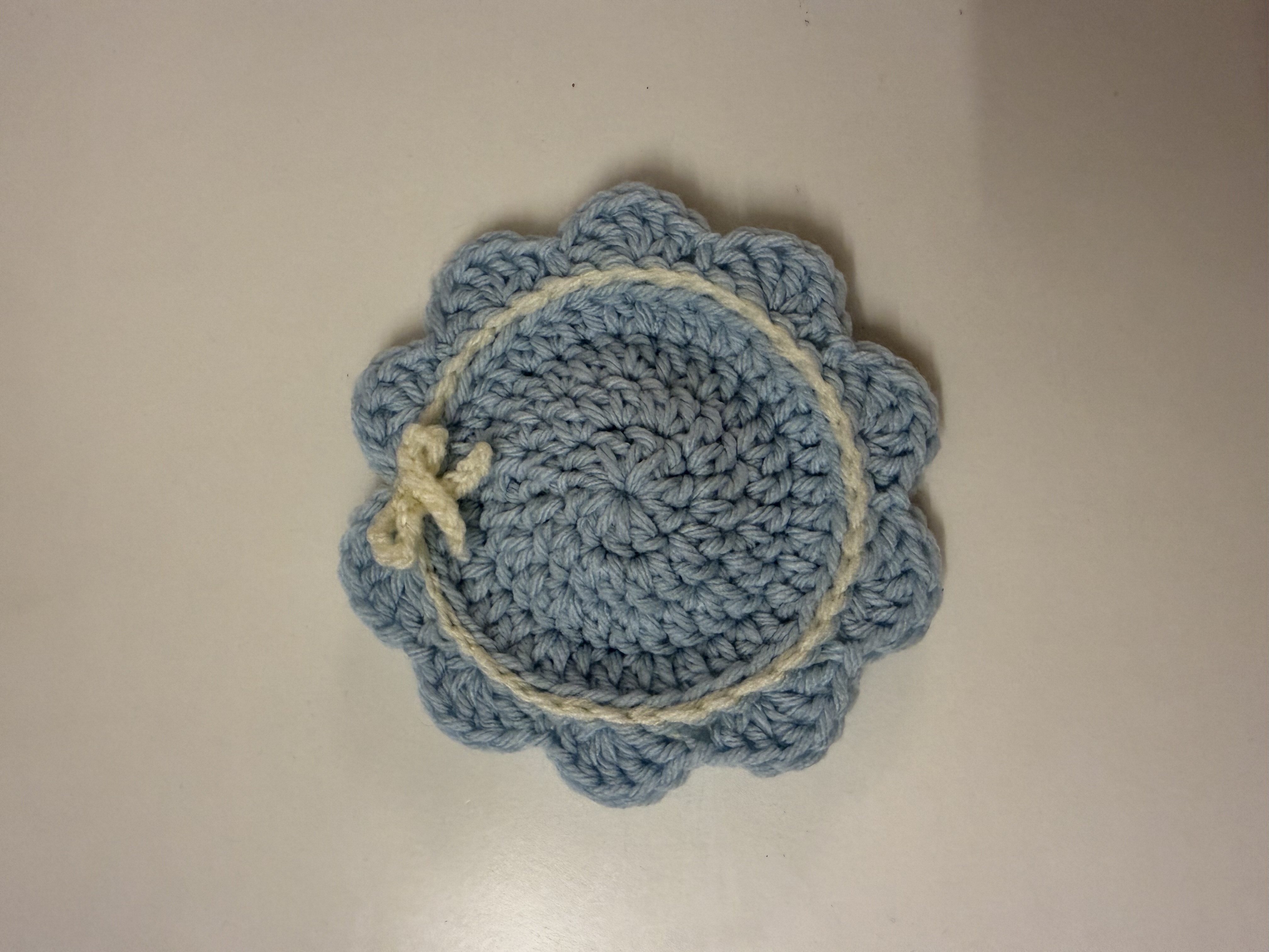 Handmade crochet flower coaster in soft blue with scalloped edge and cream bow