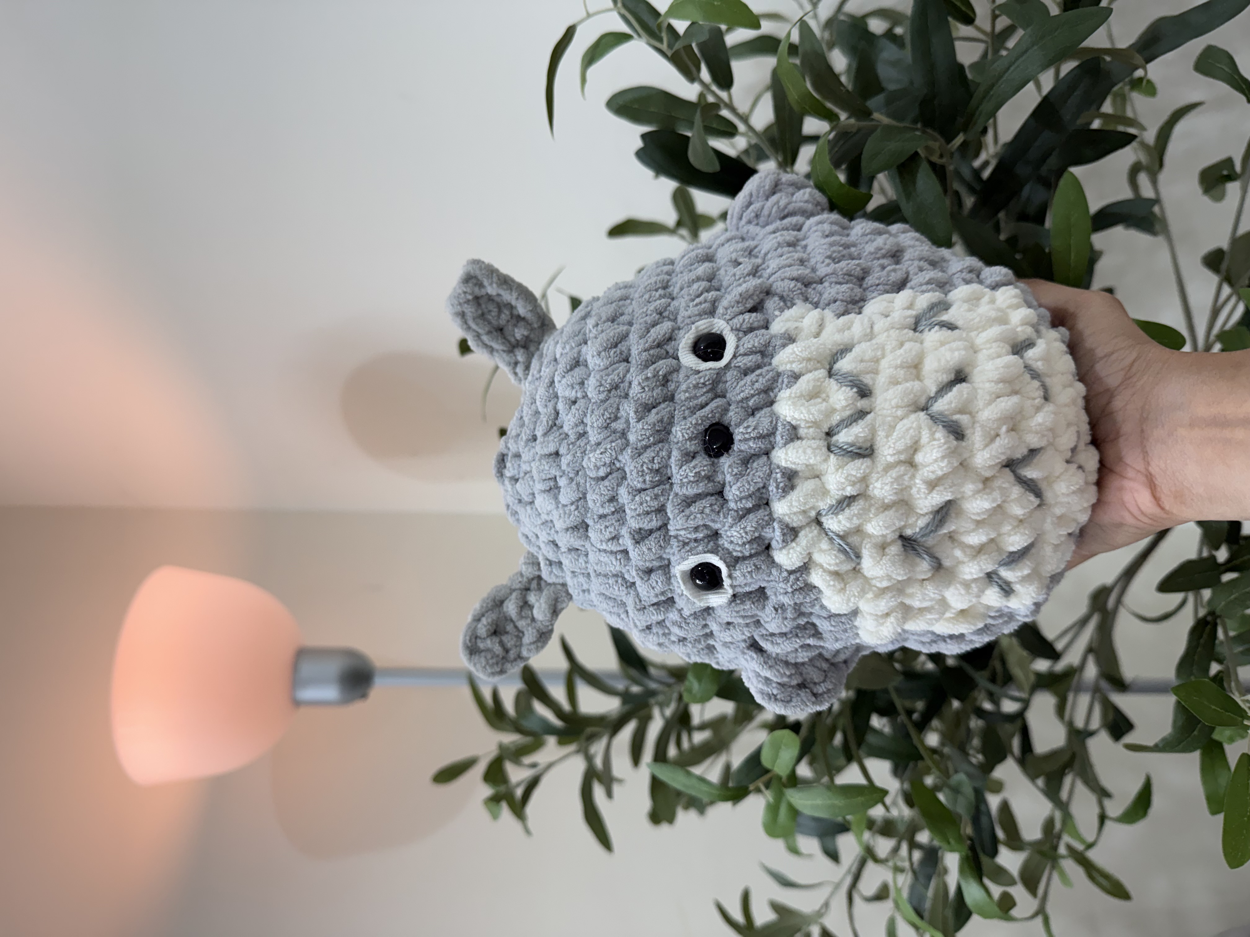 Handcrafted crochet Totoro plushie held up against green foliage