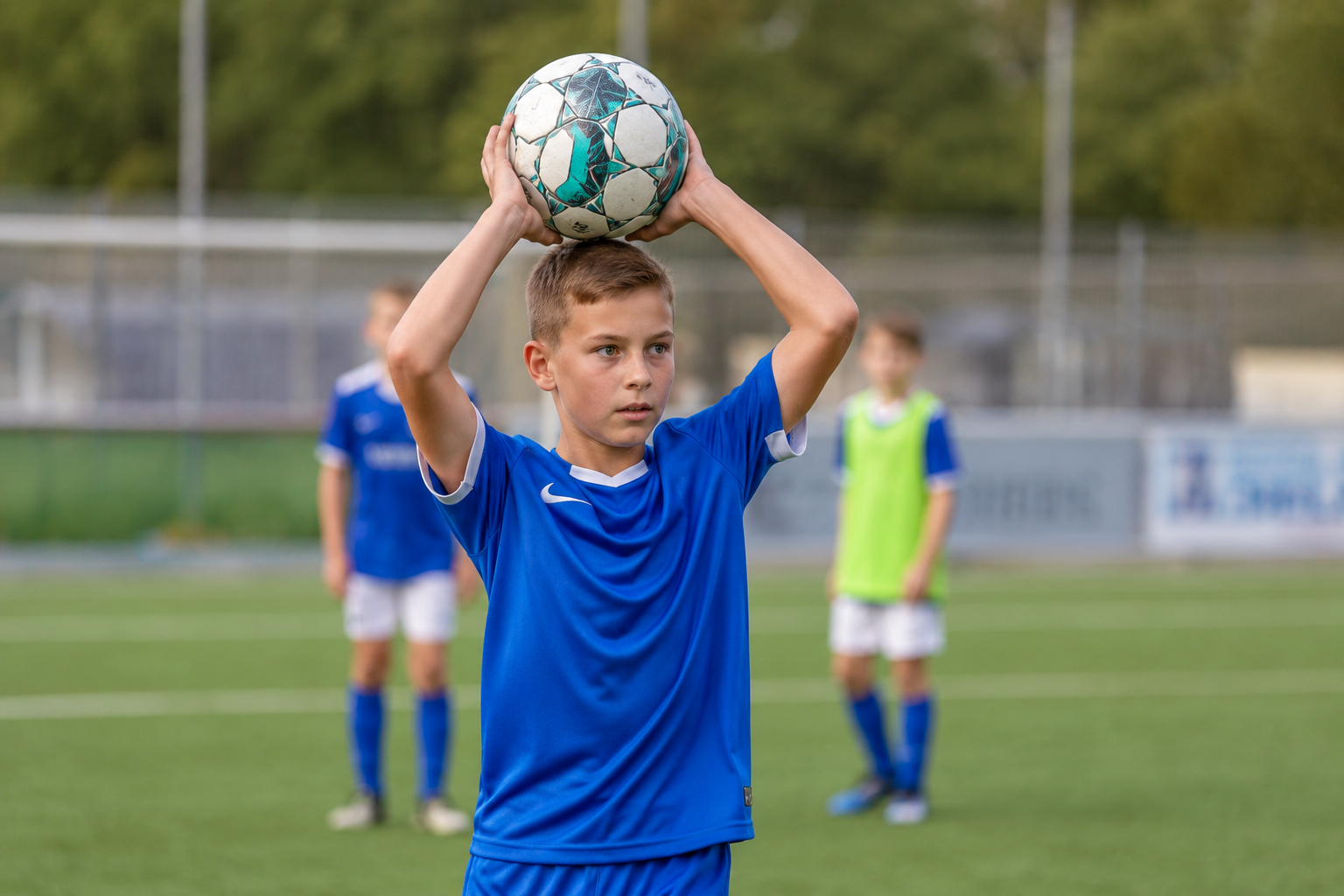 Kind beim Fußballtraining führt einen regelgerechten Einwurf mit dem Ball über dem Kopf auf einem Fußballplatz aus.