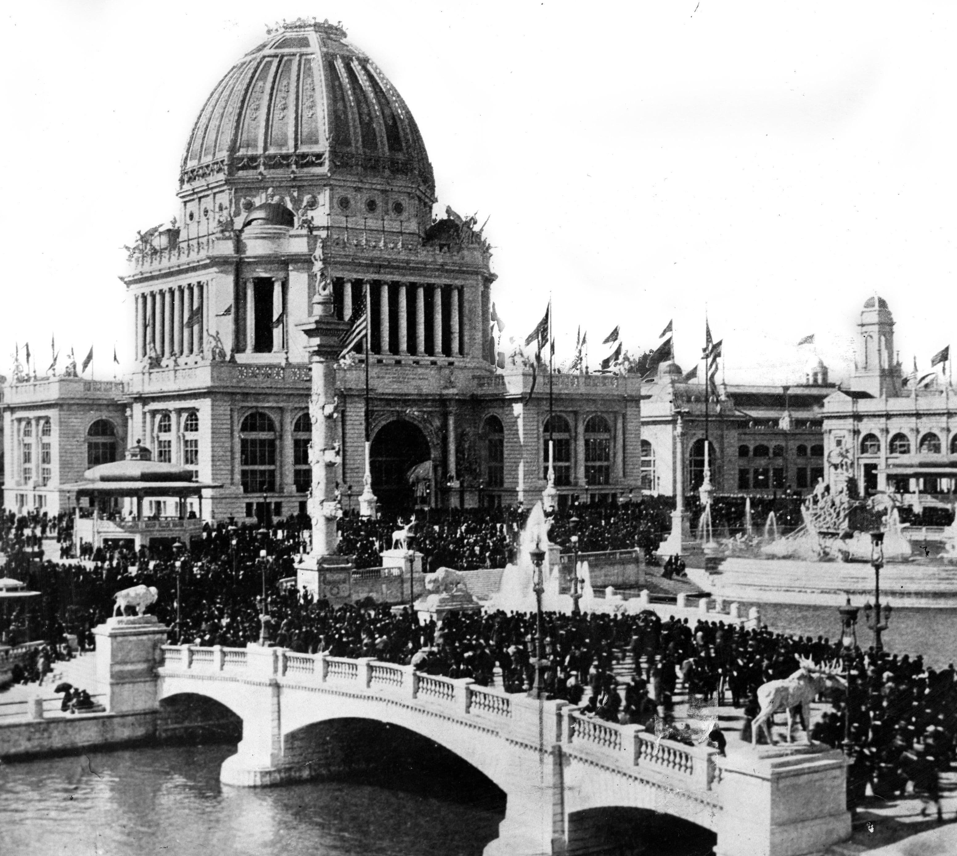 Black and White Photograph of a Crowded Bridge Leading to a Large Domed Neoclassical Building (1893)
