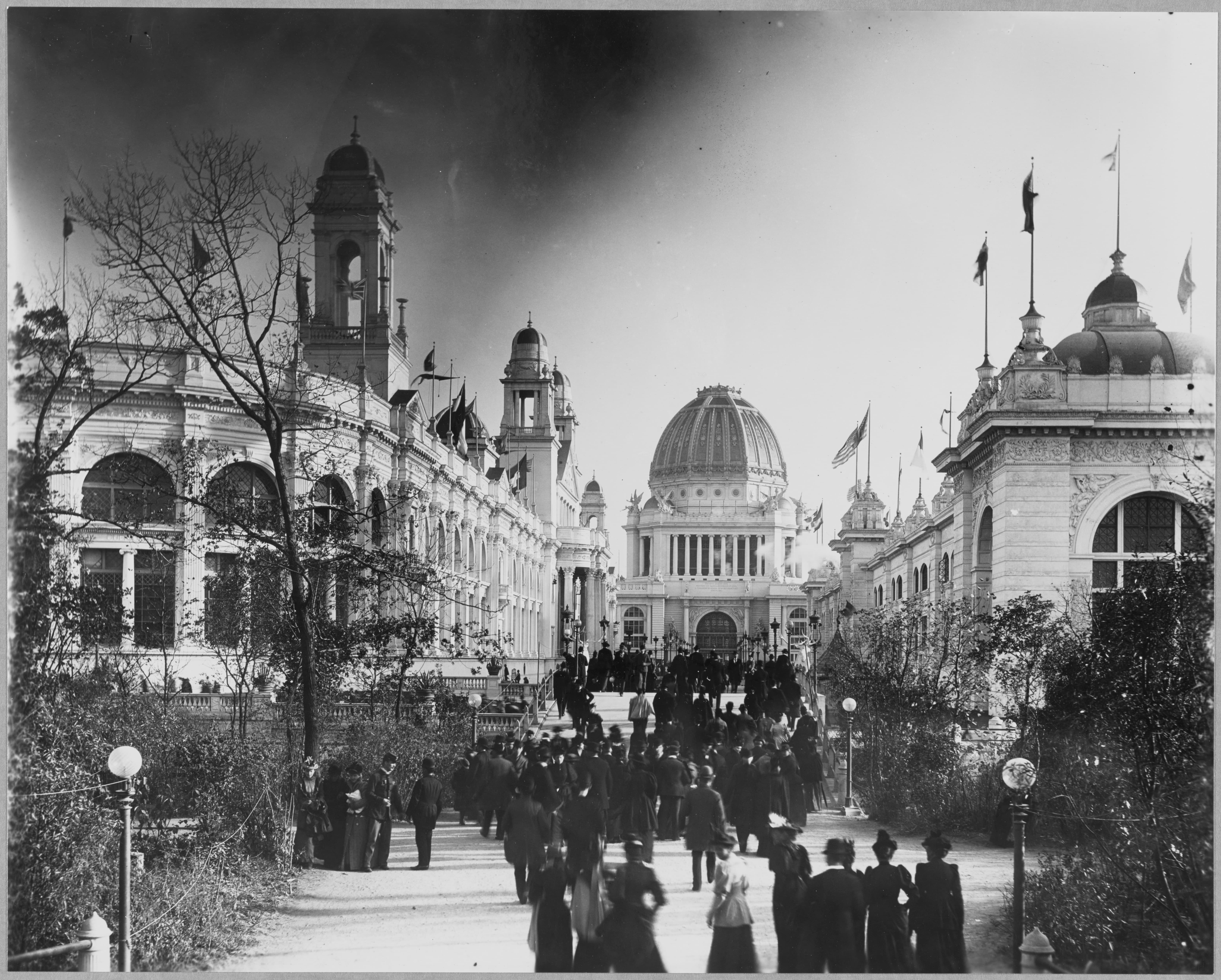 Black and white photograph of a large crowd walking toward a central domed building flanked by neoclassical exhibition halls (1893)
