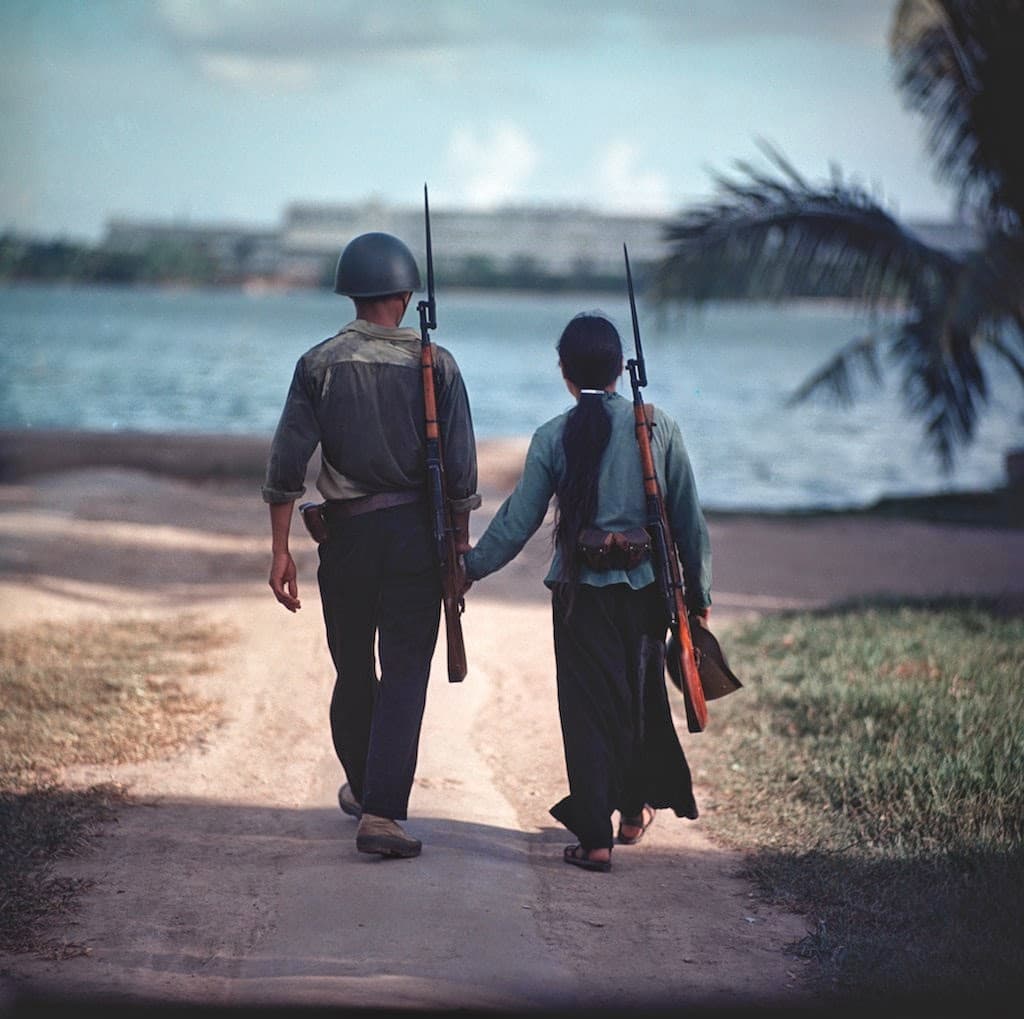 A young couple, armed with rifles, walk along the shore of the Perfume River, Hue. by Philip Jones Griffiths (1968)