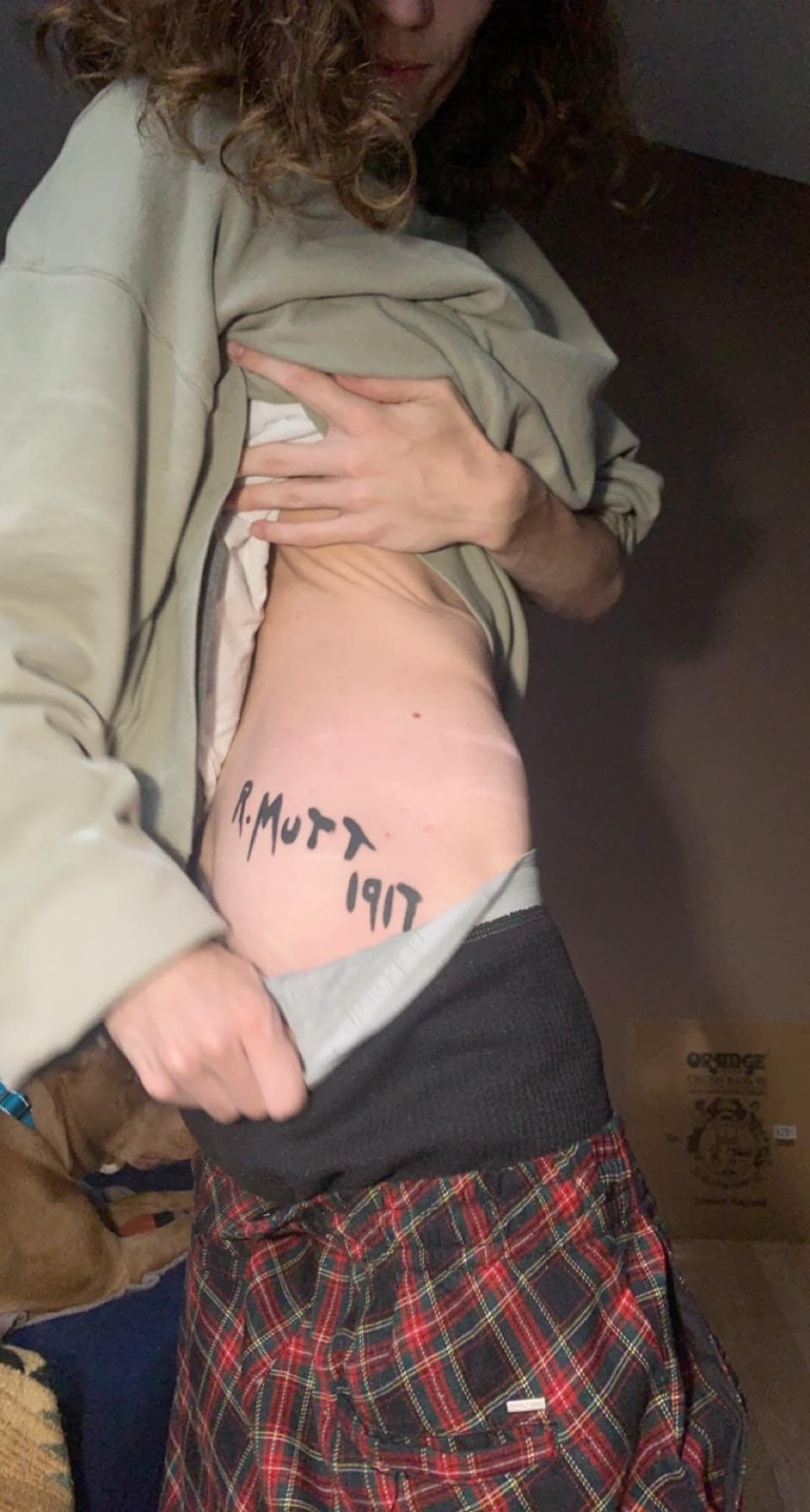 Photograph of a person revealing a tattoo reading "R. MUTT 1917" on their torso