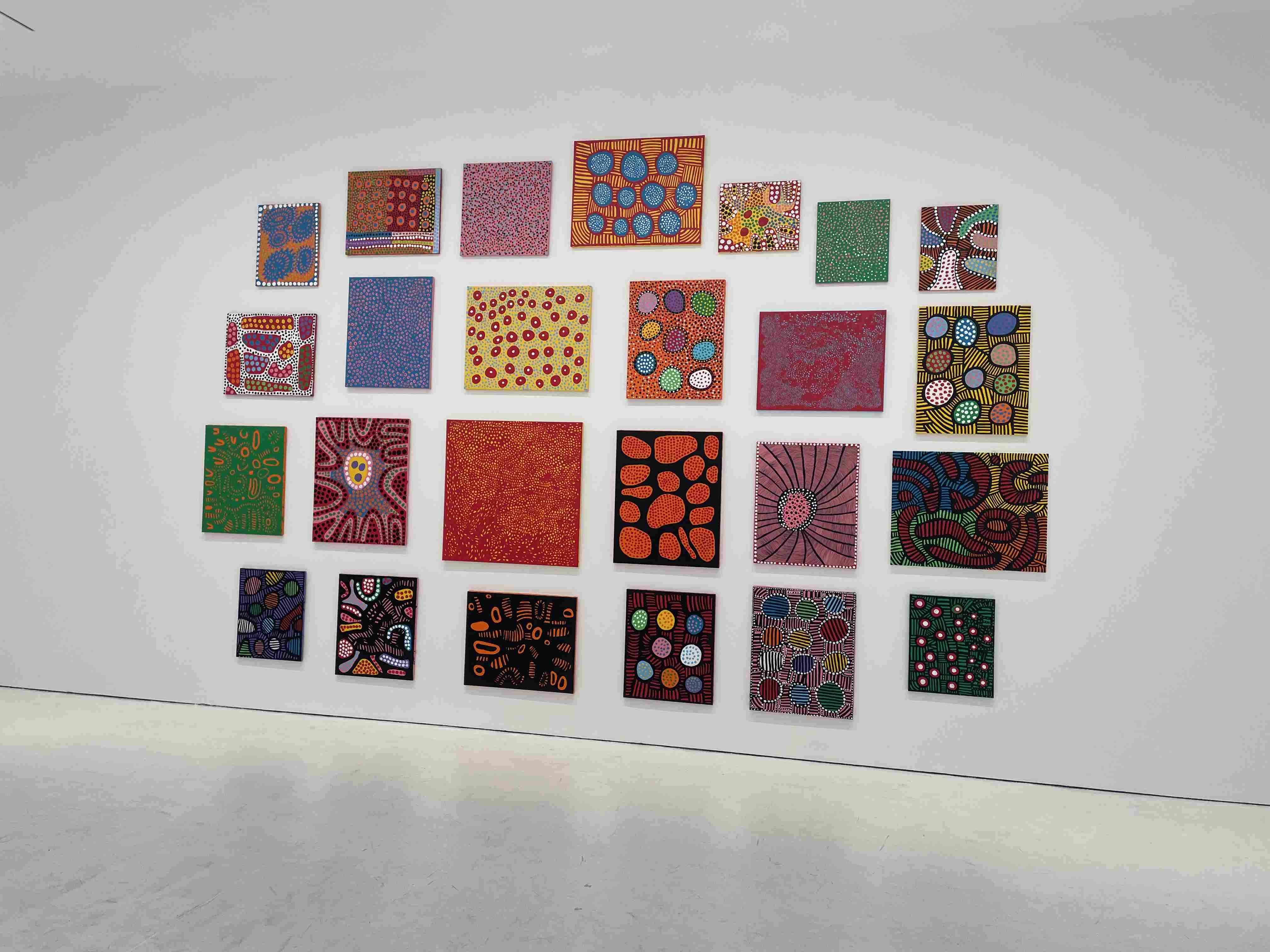 Installation of multiple square abstract paintings featuring colorful dots and patterns