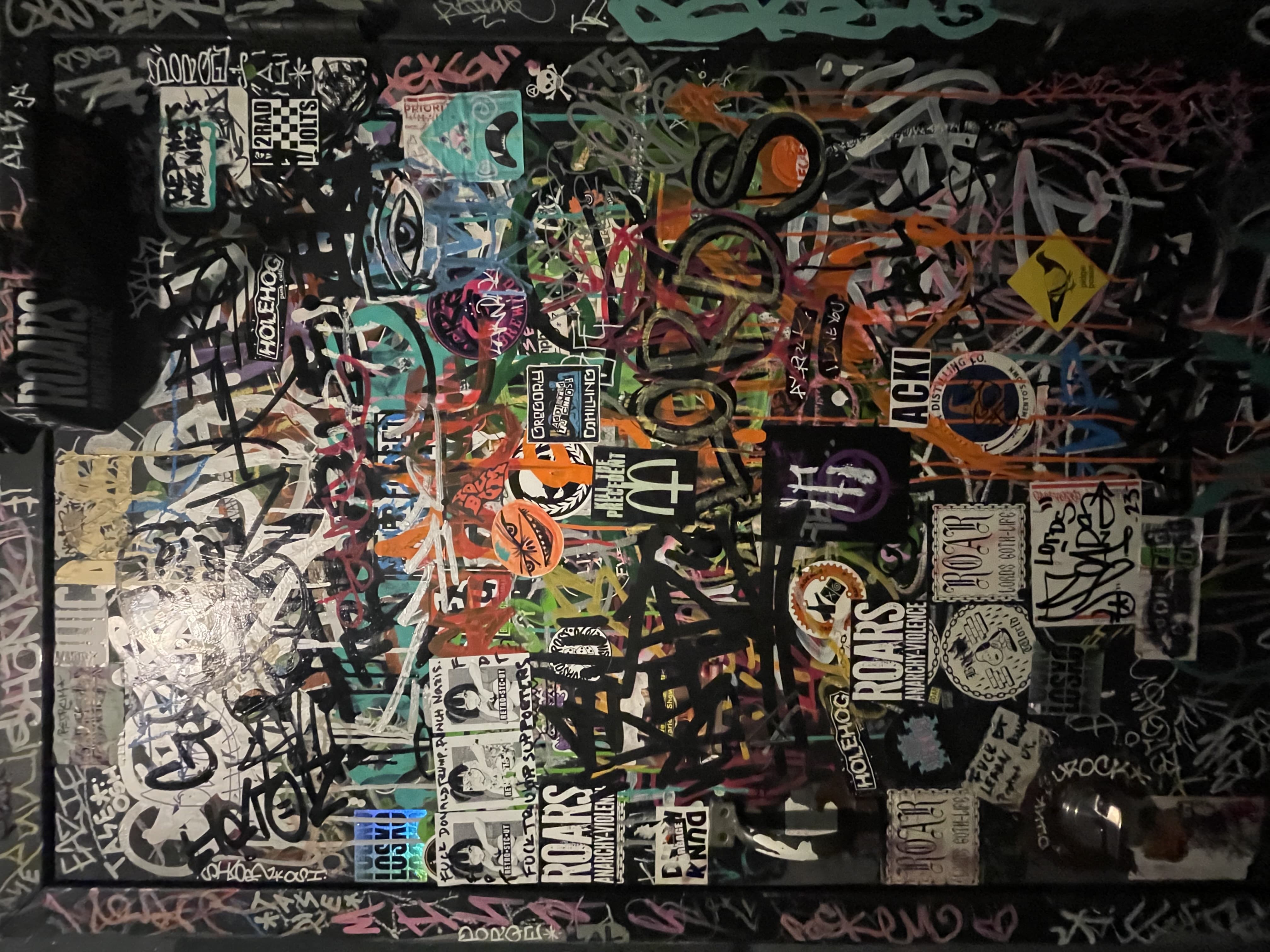 Accumulation of Graffiti Tags, Paint, and Stickers on a Black Surface