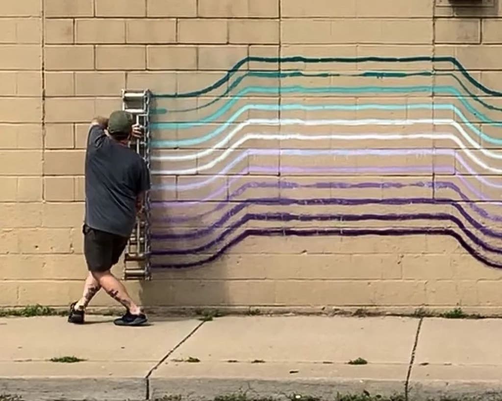 Mural in progress of horizontal colored lines on a brick wall