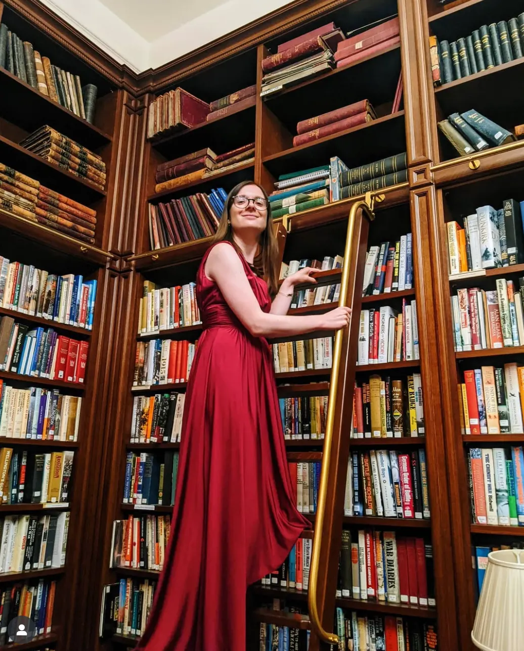 Rachel climbing a ladder to reach a high bookshelf