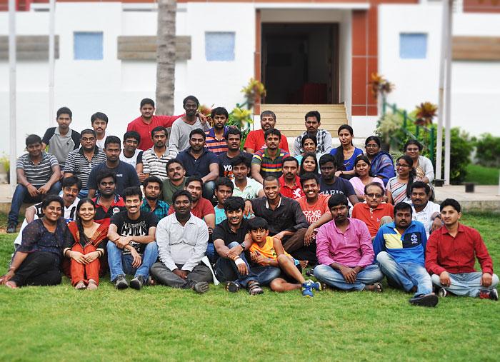 Group photograph of Mahiti Infotech team members seated and standing outdoors on a lawn in front of a building.