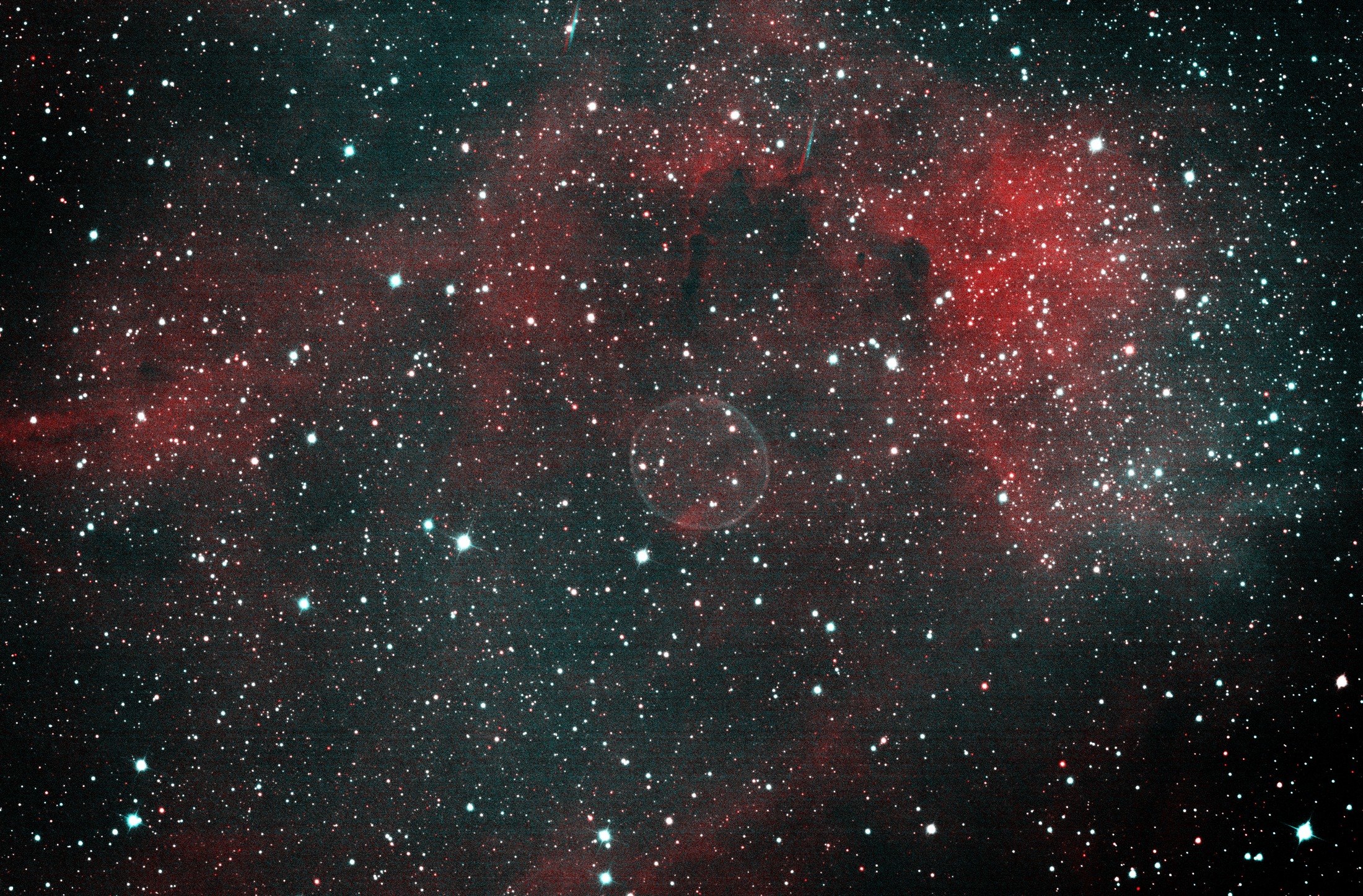 The Soap Bubble Nebula: a faint teal spherical shell left of centre in a wide field of red hydrogen emission and dense stars in Cygnus