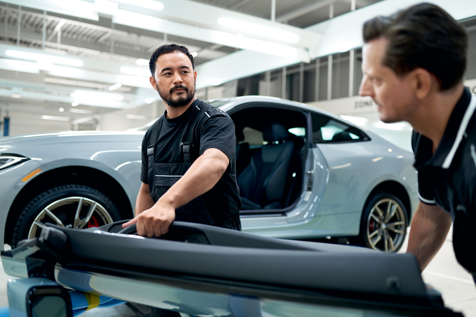 BMW technicians handling a removed door panel during collision repair