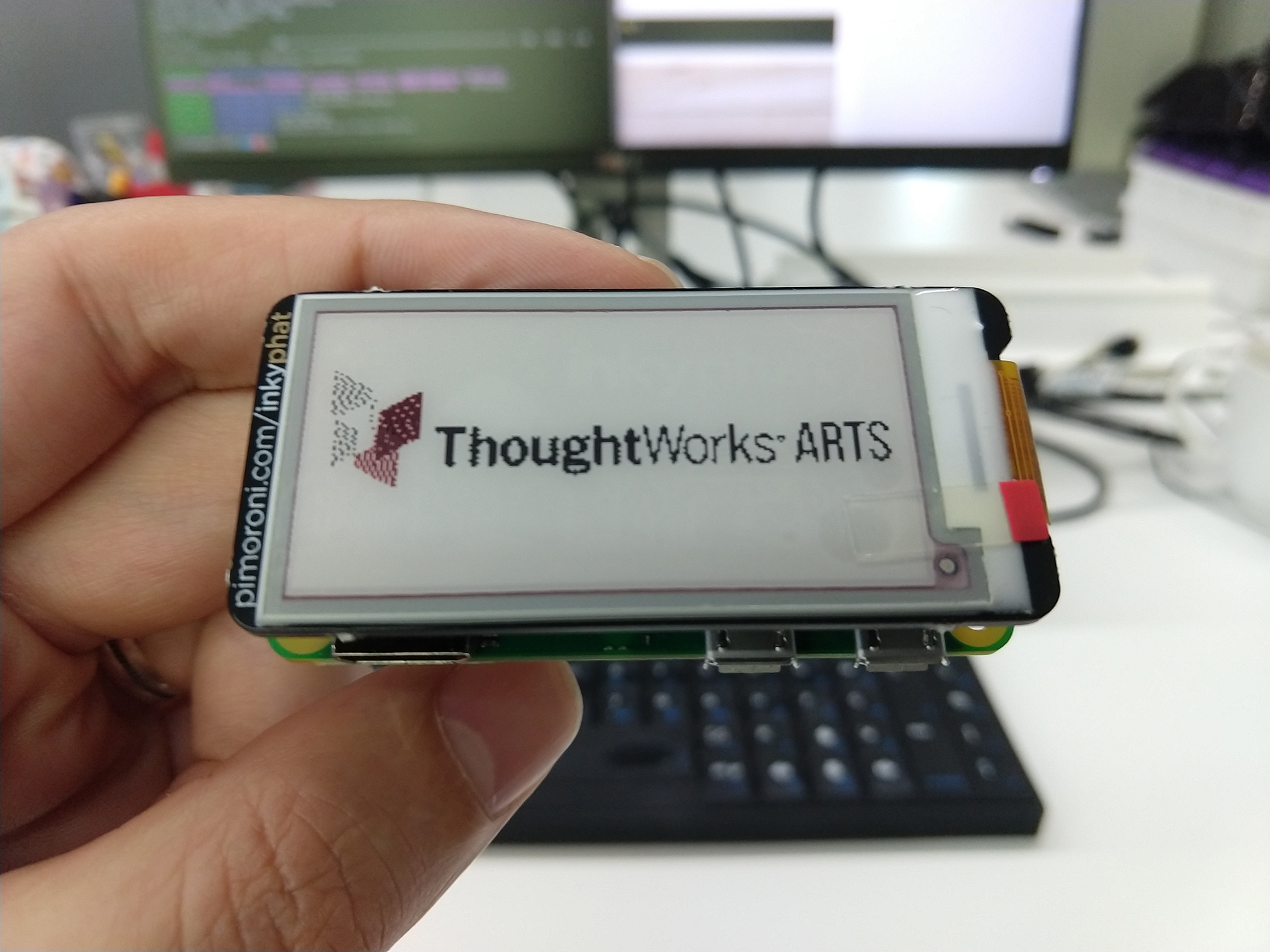 A hand holding an Inky PHAT with the ThoughtWorks Arts logo being displayed