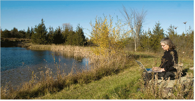 photo of woman sitting with laptop next to rural pond