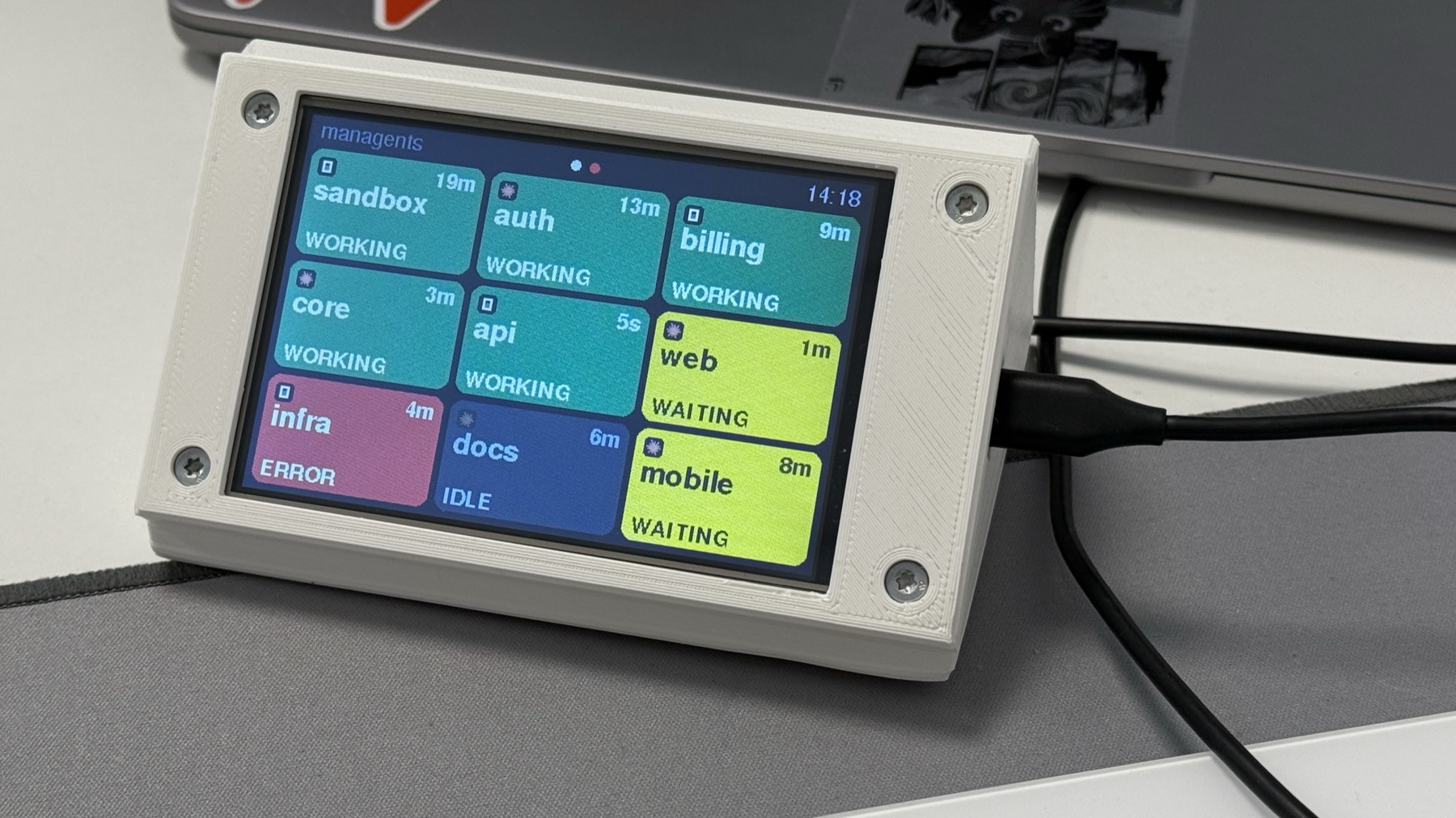 The managents display in its 3D-printed stand on a desk, showing nine agent cards