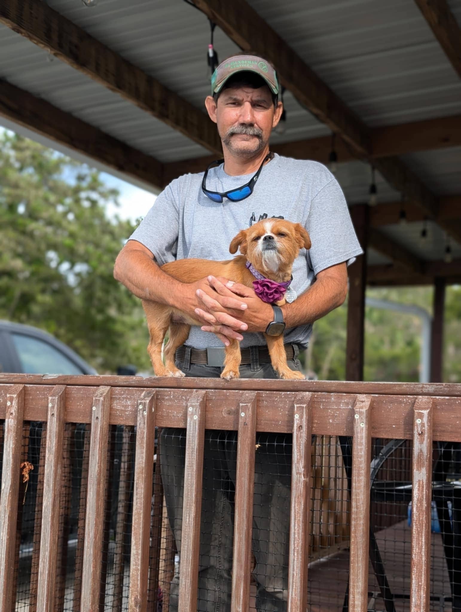Adam Lazenby gently holding a small dog on a wooden deck, showcasing his compassionate nature with animals