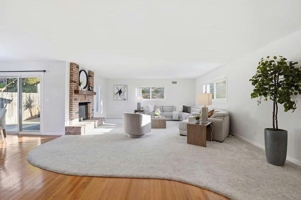 Spacious living room with brick fireplace, hardwood floors, and natural light