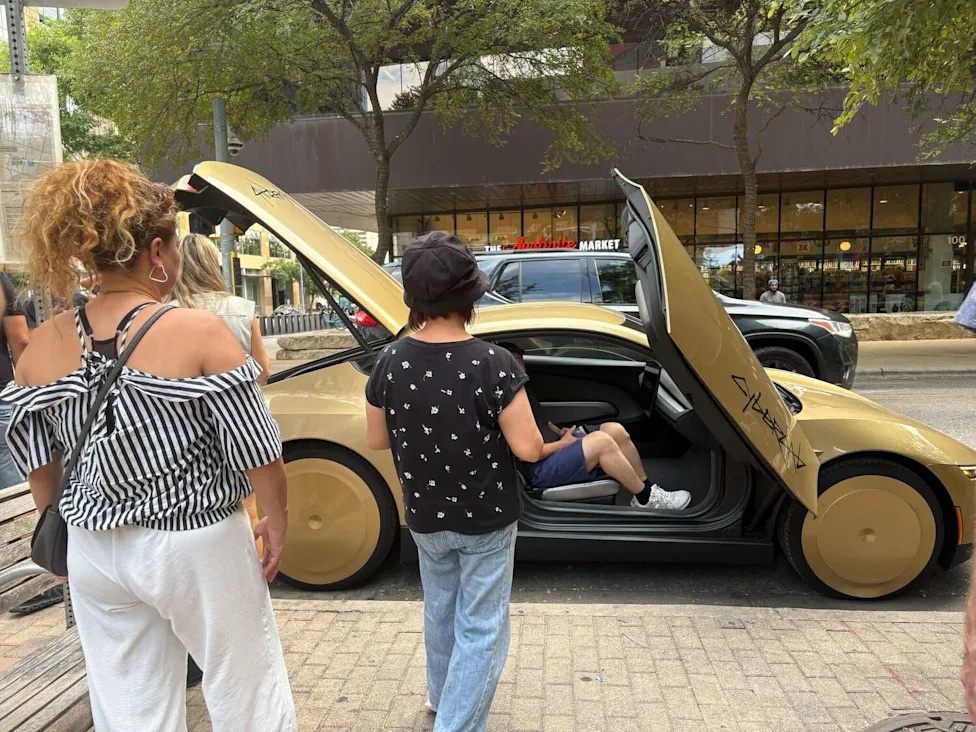 A gold Cybercab parked outside ACL Live in downtown Austin as people gather around it