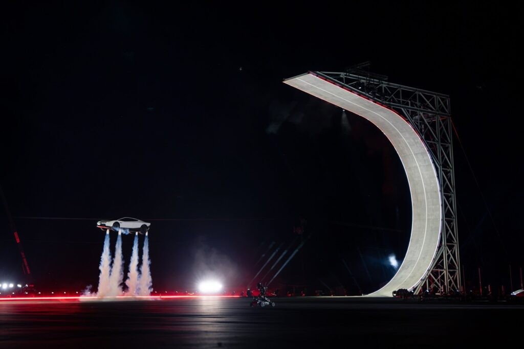 Roadster supported by visible thruster plumes beside the curved ramp