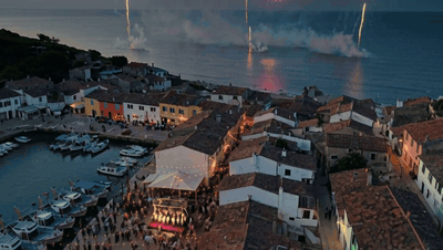 A drone glides over a fishing village festival as fireworks burst over the sea